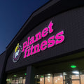 Planet Fitness gym exterior at night with bright pink neon sign.